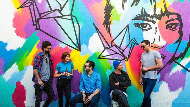 A group of people conversing in front of a colourful mural.