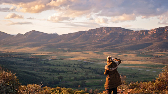 A woman standing on a hilltop overlooking the landscape and hills in the background.